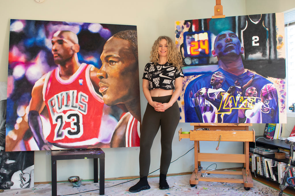 Carling Jackson standing between two paintings honoring Michael Jordan and Kobe Bryant