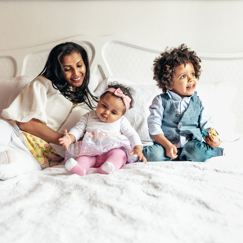 Family (Mother, infant, and toddler) playing on a bed