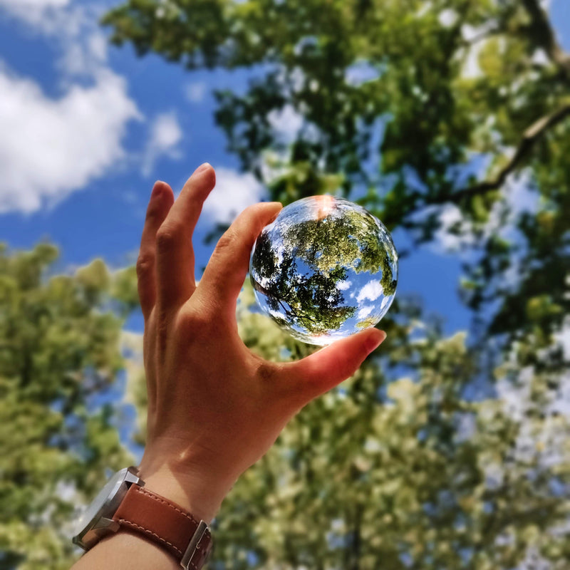Holding a glass sphere in front of green trees and a blue sky 