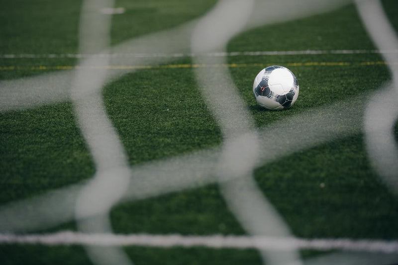 Soccer ball on a field seen through a goal net 