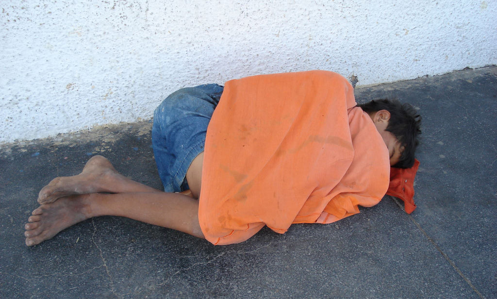 Boy sleeping on the street under a sweater.